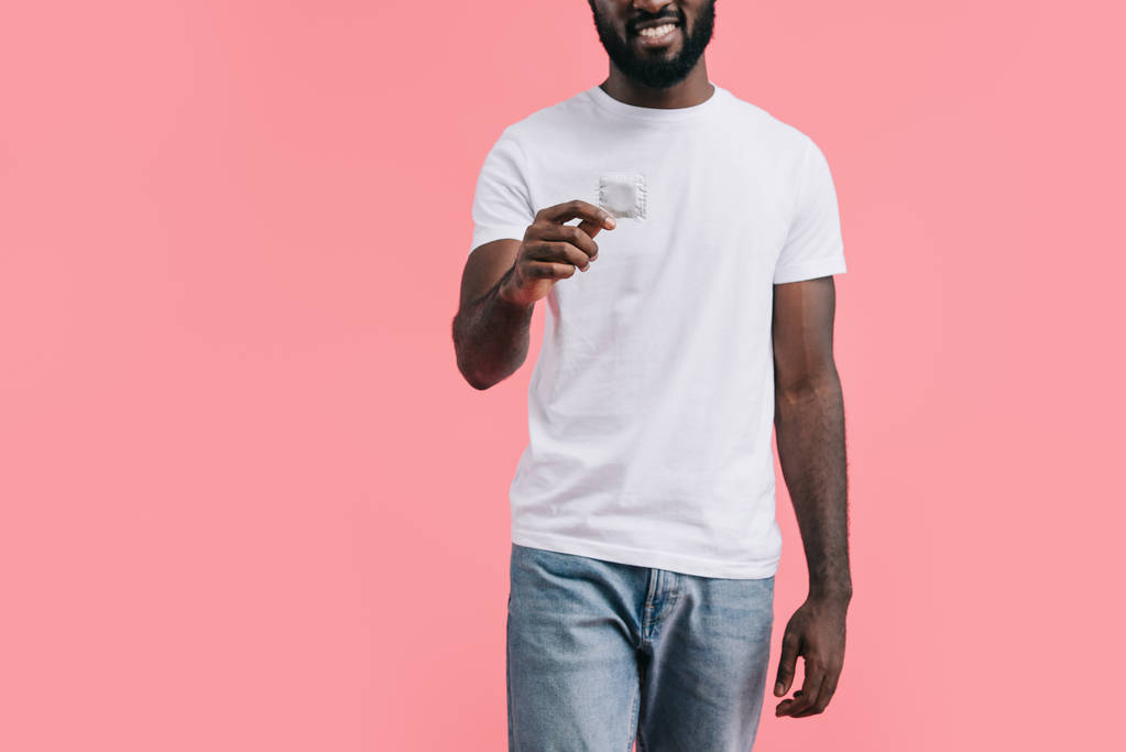 частичный взгляд молодого африканского американца с презервативом, изолированным на розовом фоне
  - Фото, изображение