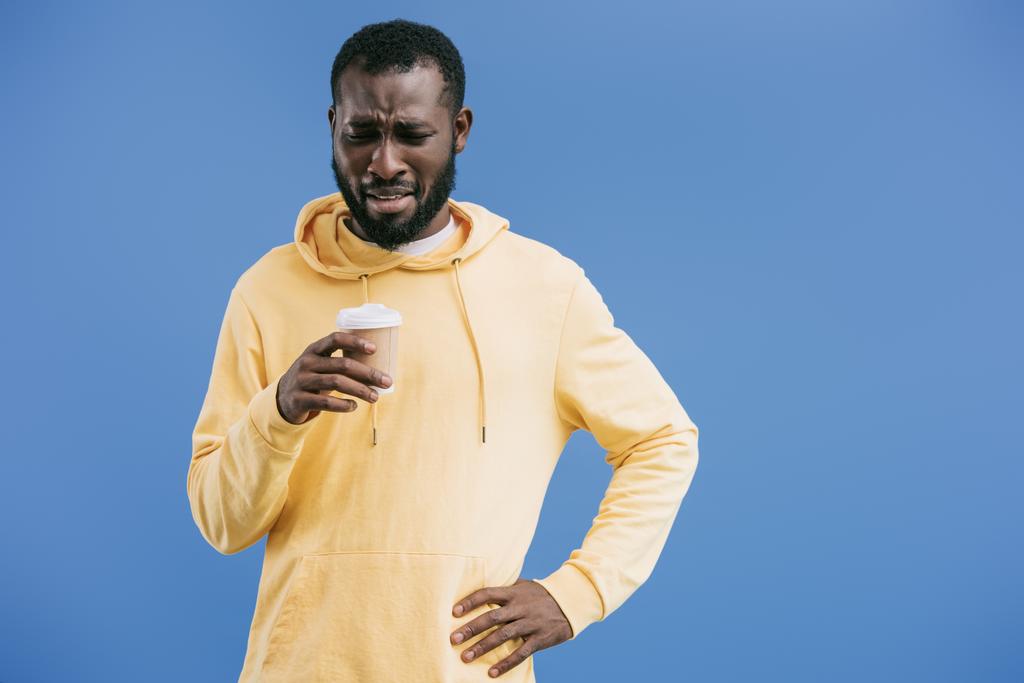 disappointed young african american man with disposable coffee cup isolated on blue background - Photo, Image