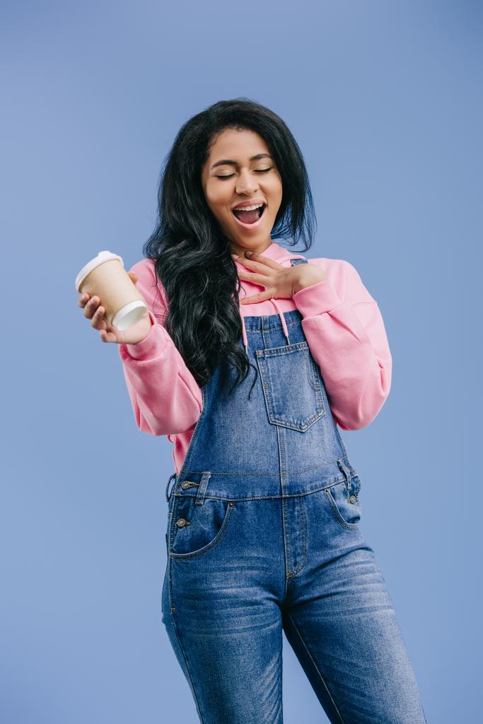 felice donna africana americana gesticolando a mano e tenendo monouso tazza di caffè isolato su sfondo blu
  - Foto, immagini