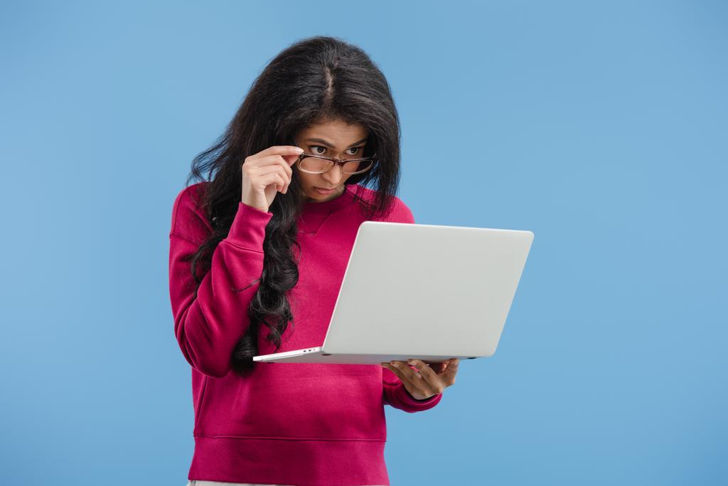 зосереджена молода афроамериканка в окулярах дивиться на ноутбук ізольовано на синьому фоні
  - Фото, зображення