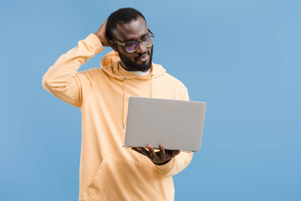 nachdenkliche junge afrikanisch-amerikanische Mann mit Brille Blick auf Laptop isoliert auf blauem Hintergrund - Foto, Bild