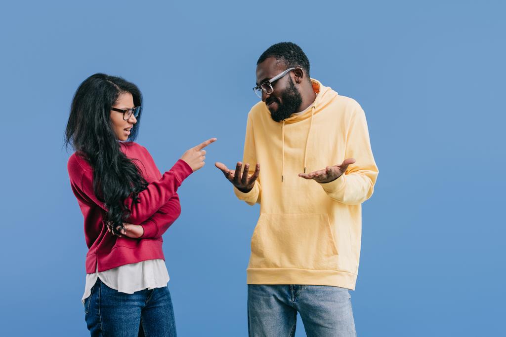 mujer afroamericana enojada señalando con el dedo al novio haciendo gesto de encogimiento aislado sobre fondo azul
  - Foto, imagen