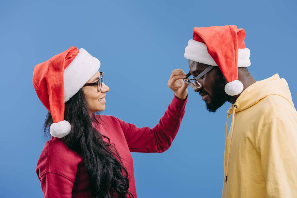ピンクの背景に分離された彼氏からメガネを脱いでクリスマス帽子の若いアフリカ系アメリカ人女性の側面図  - 写真・画像