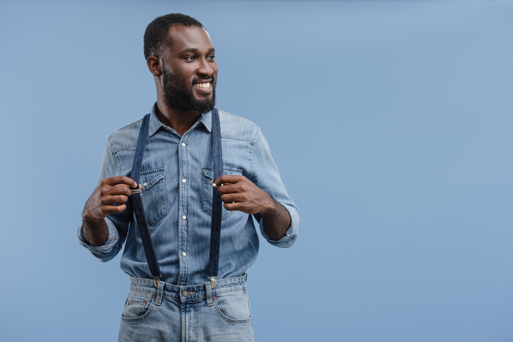стильный молодой африканский американец касаясь подтяжки изолированы на синем фоне
 - Фото, изображение
