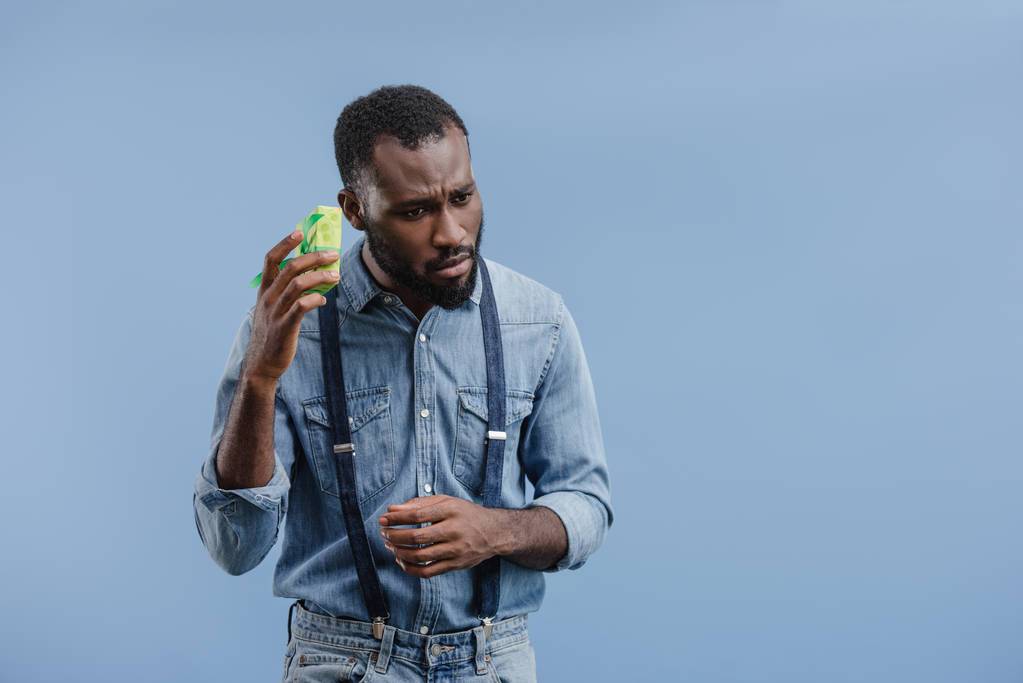 töprengő fiatal afroamerikai férfi, ajándékdobozba csomagolva szalag kék háttér elszigetelt hallgat - Fotó, kép