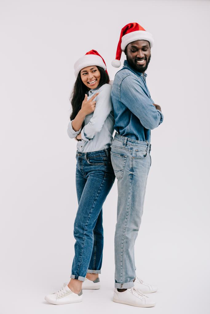 χαμογελώντας αφρικανική αμερικανική ζευγάρι σε καπέλα santa στέκεται απομονωθεί σε λευκό στην πίσω - Φωτογραφία, εικόνα