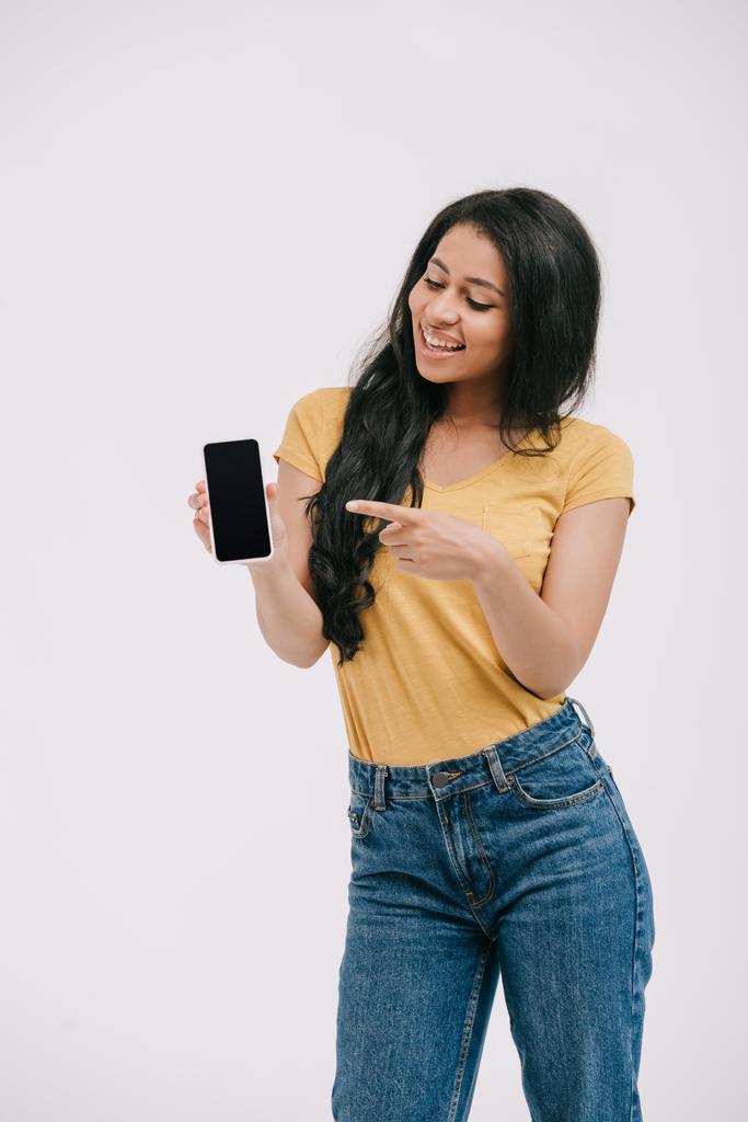 Gelukkig Afrikaans Amerikaans meisje wijzen op smartphone met leeg scherm geïsoleerd op wit - Foto, afbeelding