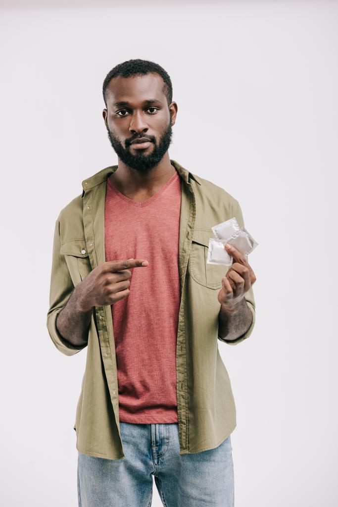 ernstige knappe Afro-Amerikaanse man die wijzen op condooms geïsoleerd op wit - Foto, afbeelding