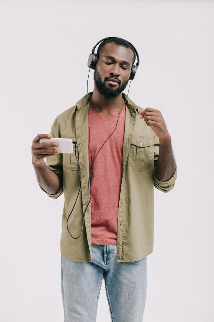 schöner afrikanisch-amerikanischer Mann hört Musik mit Smartphone und Kopfhörer isoliert auf weiß - Foto, Bild