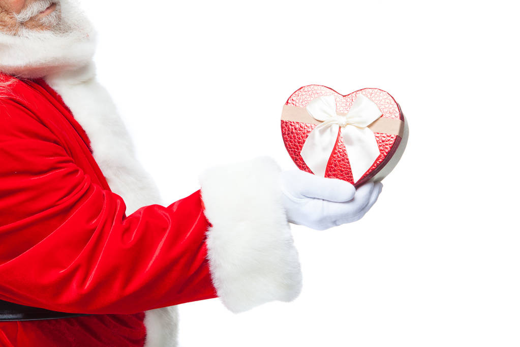 Vánoce. Santa Claus v bílých rukavicích drží červené srdce ve tvaru krabičky s bílou mašlí. Izolované na bílém pozadí. Detailní záběr - Fotografie, Obrázek