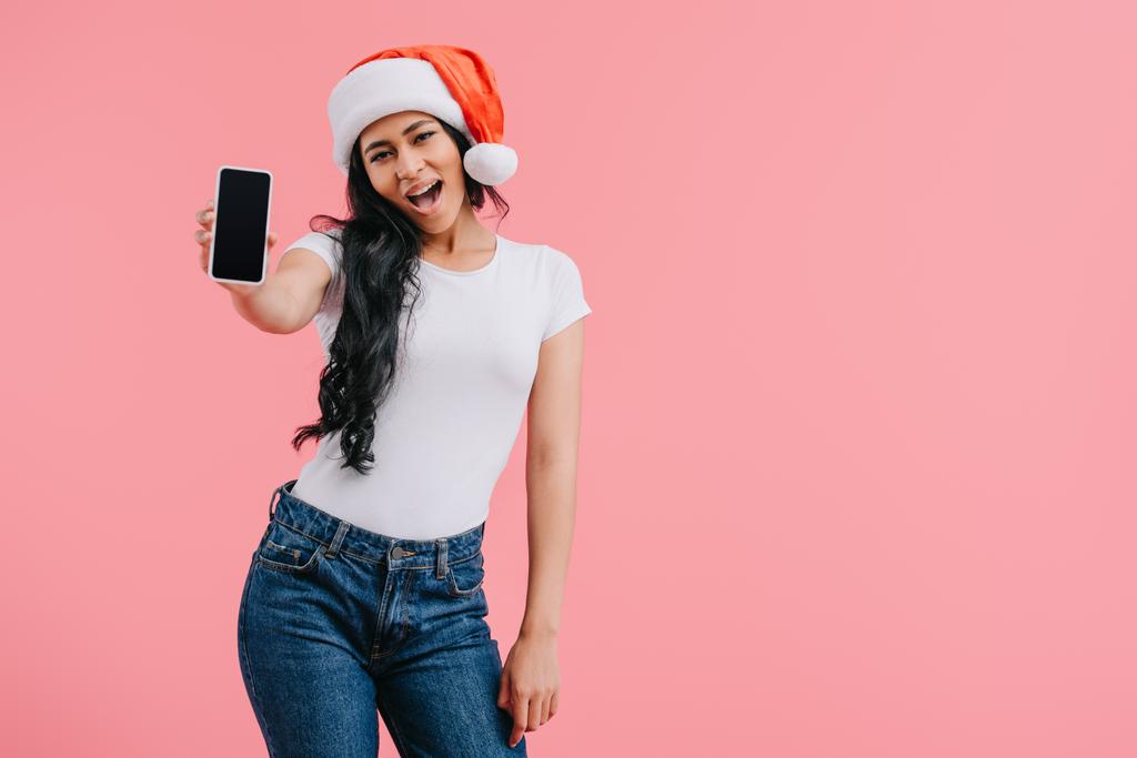 aufgeregt attraktive afrikanisch-amerikanische Mädchen in Hosen Hut zeigt Smartphone mit leerem Bildschirm isoliert auf rosa - Foto, Bild