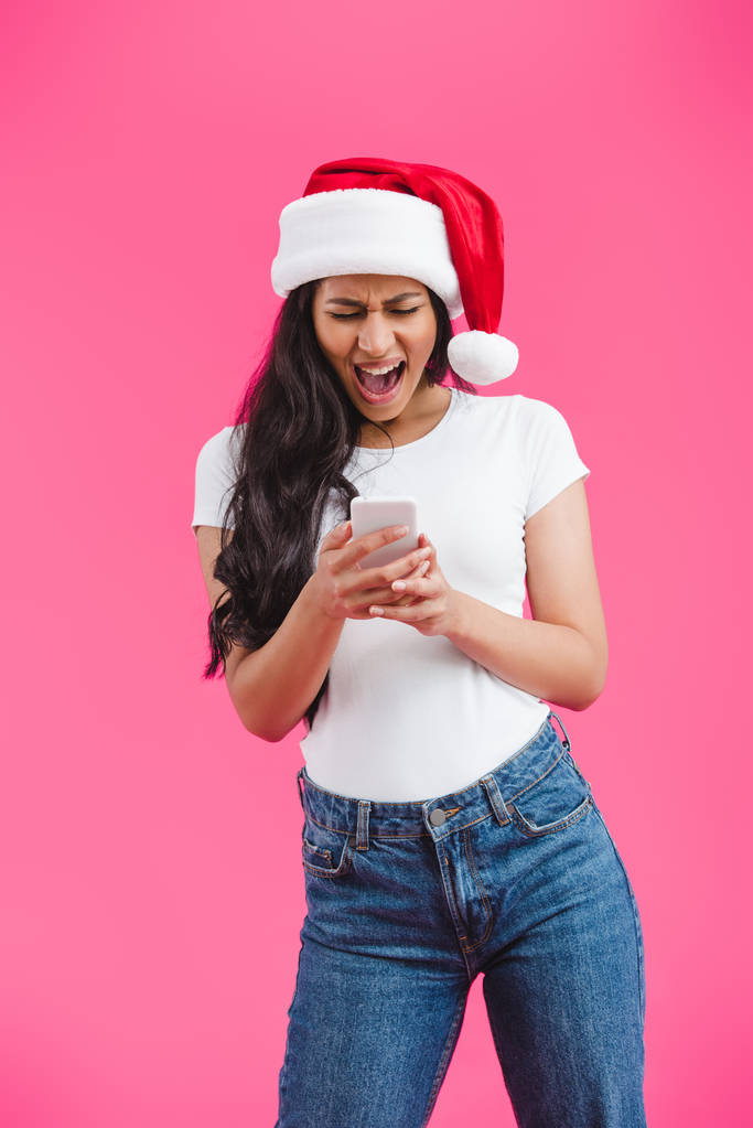 african american girl in santa hat screaming and looking at smartphone isolated on pink - Photo, Image