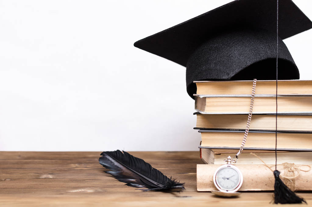 Стопка книг, дипломная шапка, диплом и карманные часы на школьном столе изолированы на белом фоне
. - Фото, изображение