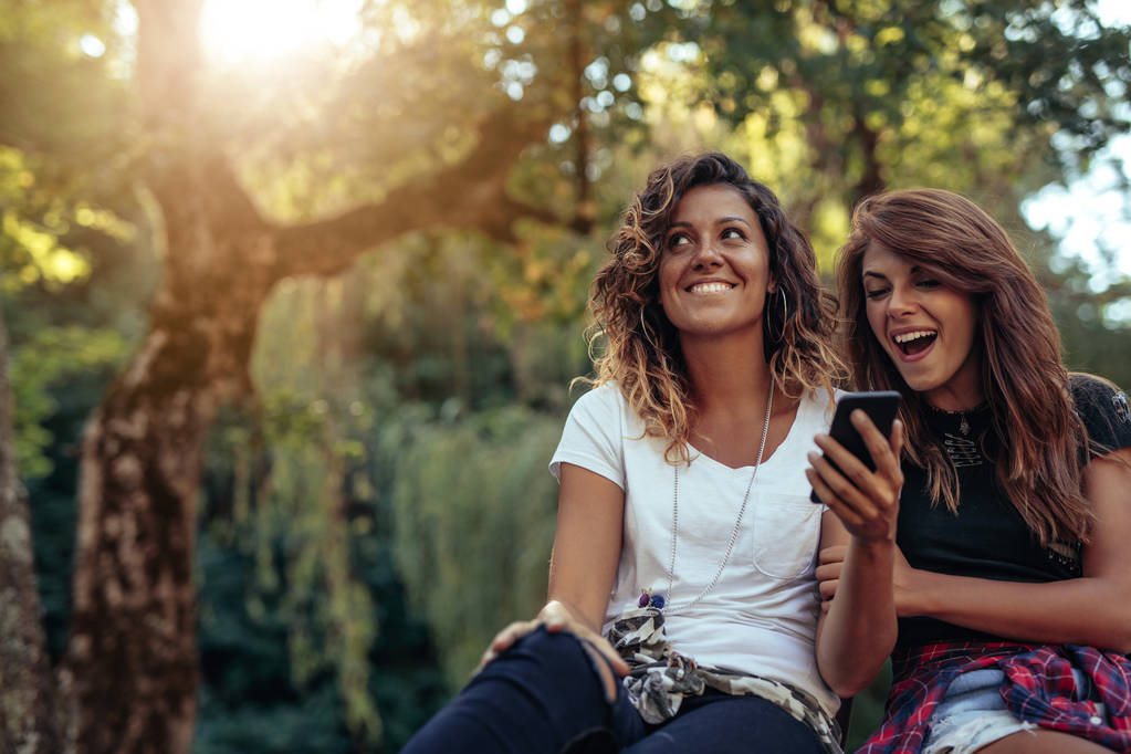 Deux jeunes filles assises dans un parc regardant un téléphone portable
 - Photo, image