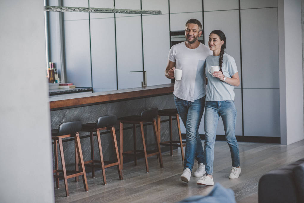 sonriente pareja con tazas de café en la cocina en casa
  - Foto, imagen