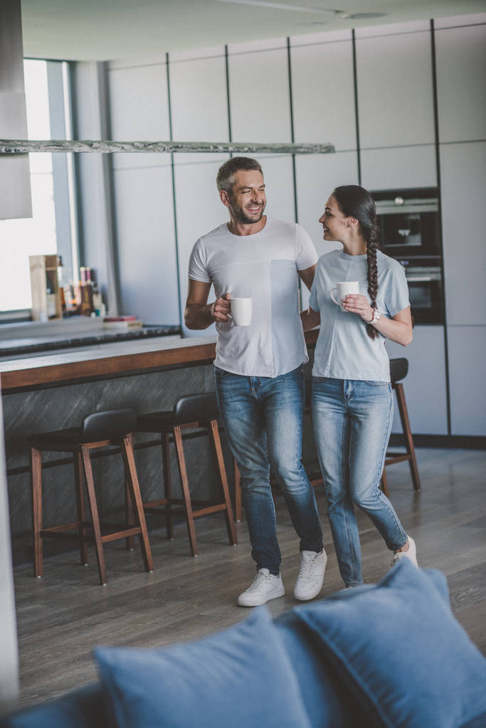 happy couple with coffee cups talking in kitchen at home  - Photo, Image