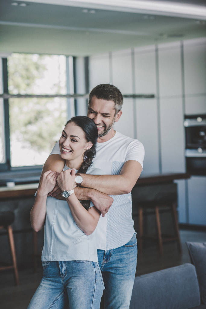 riendo hombre abrazando novia por detrás en cocina en casa
 - Foto, imagen