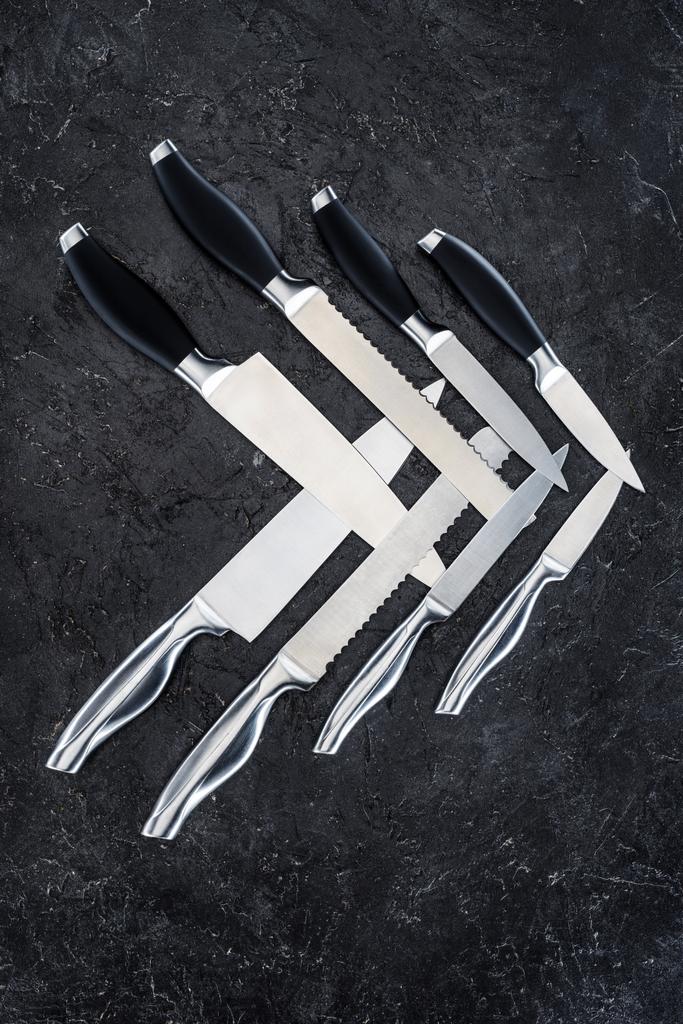 σύνολο των διαφόρων μαχαίρια κουζίνας που διοργανώνονται στη μαύρη επιφάνεια, το top view   - Φωτογραφία, εικόνα