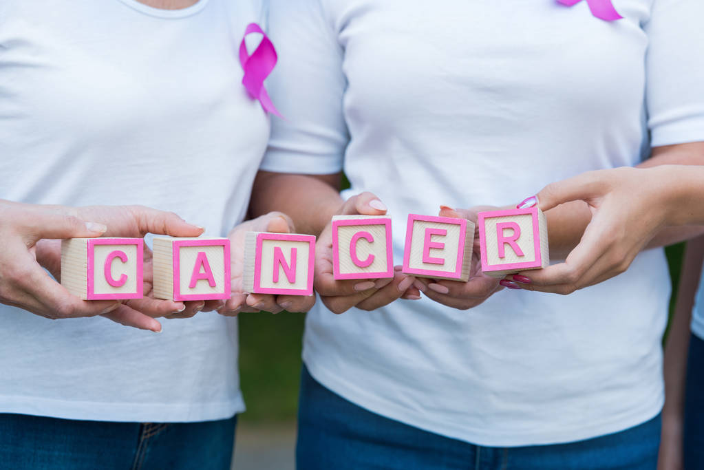 plan recadré de femmes avec des rubans de sensibilisation au cancer du sein tenant des cubes avec le mot cancer
 - Photo, image