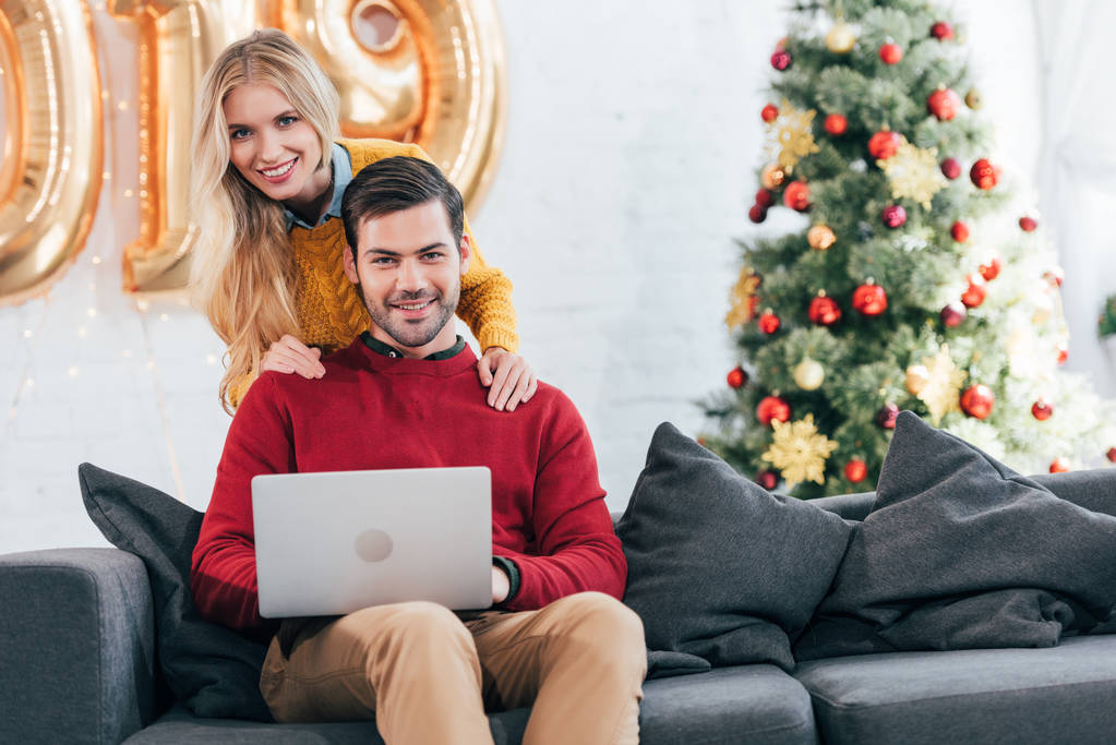 smiling couple using laptop together at home with christmas tree - Photo, Image