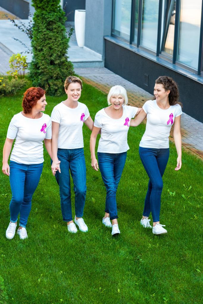 vue grand angle de quatre femmes souriantes avec des rubans de sensibilisation au cancer du sein marchant ensemble
  - Photo, image