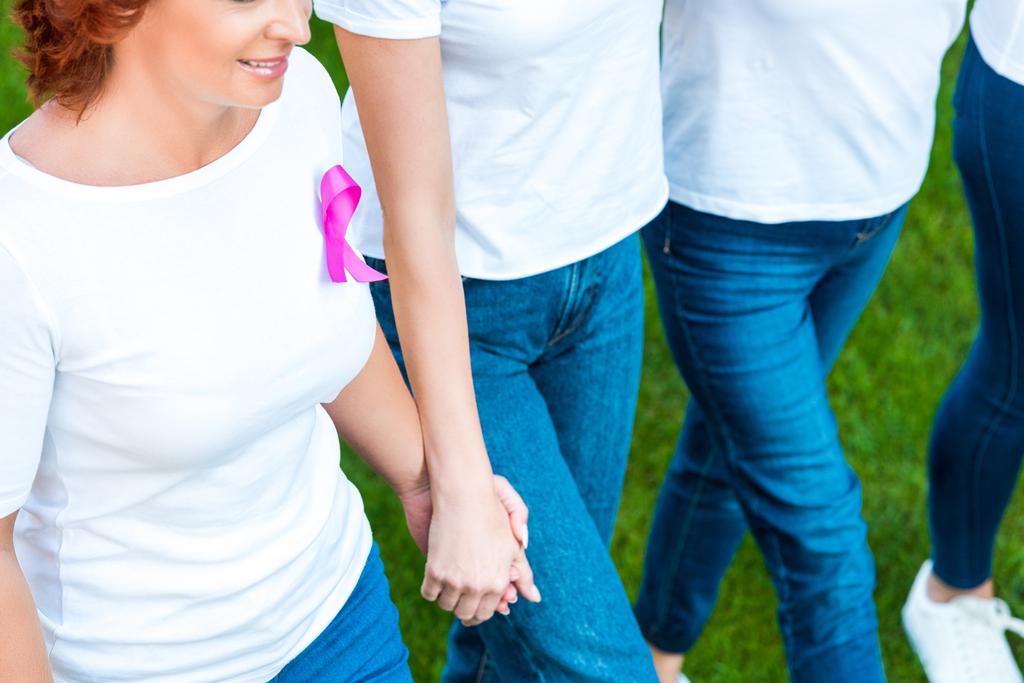 cropped shot of women holding hands and walking on lawn, breast cancer awareness concept - Photo, Image