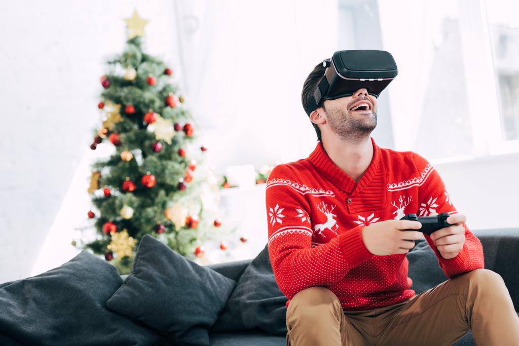 Aufgeregter Mann spielt an Heiligabend Spiel mit Virtual-Reality-Headset und Joy-Pad - Foto, Bild