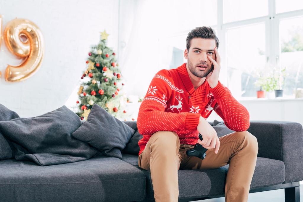 ideges ember tartja a botkormány és karácsonyfa mögött kanapén ül - Fotó, kép