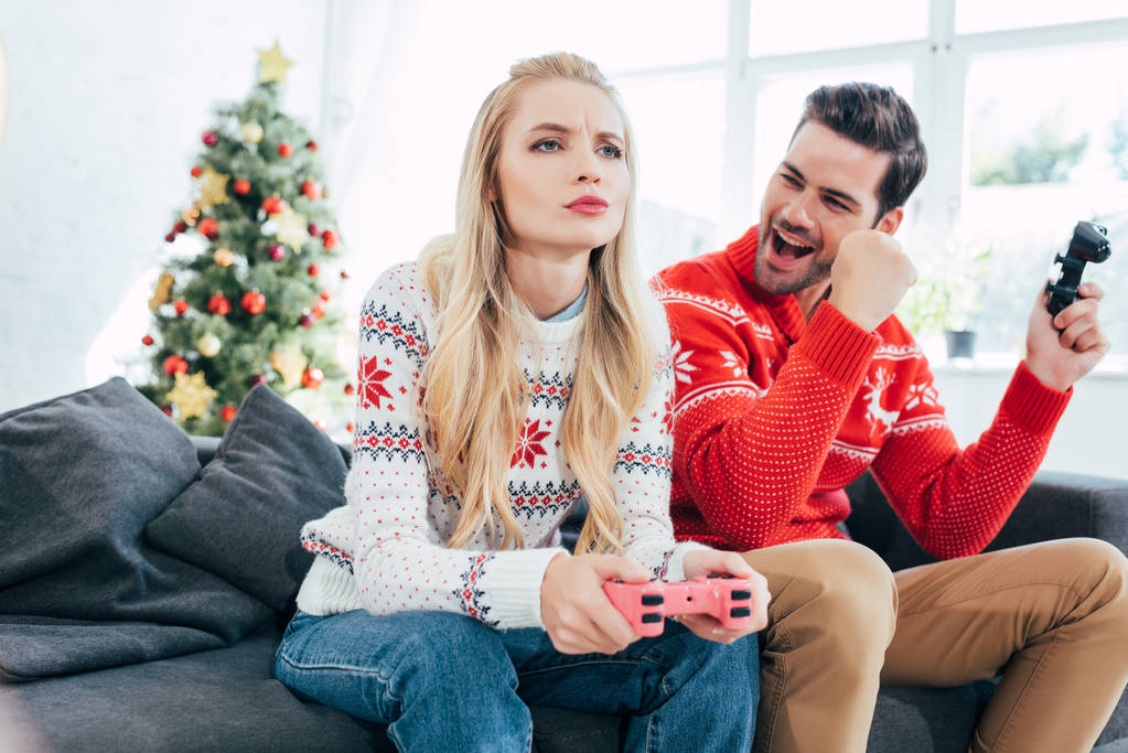 若い夫婦 カップル ビデオ ゲームのクリスマス ツリーでジョイスティックを自宅で ロイヤリティフリー写真 画像素材