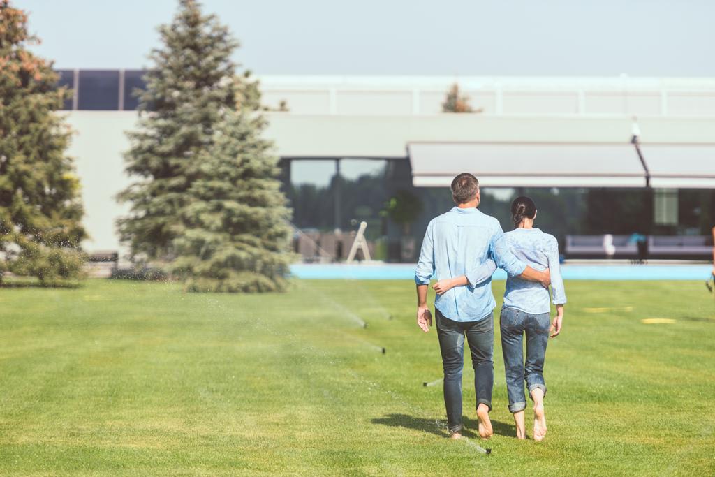 vista posteriore della coppia che si abbraccia e cammina sul prato vicino alla casa di campagna
  - Foto, immagini