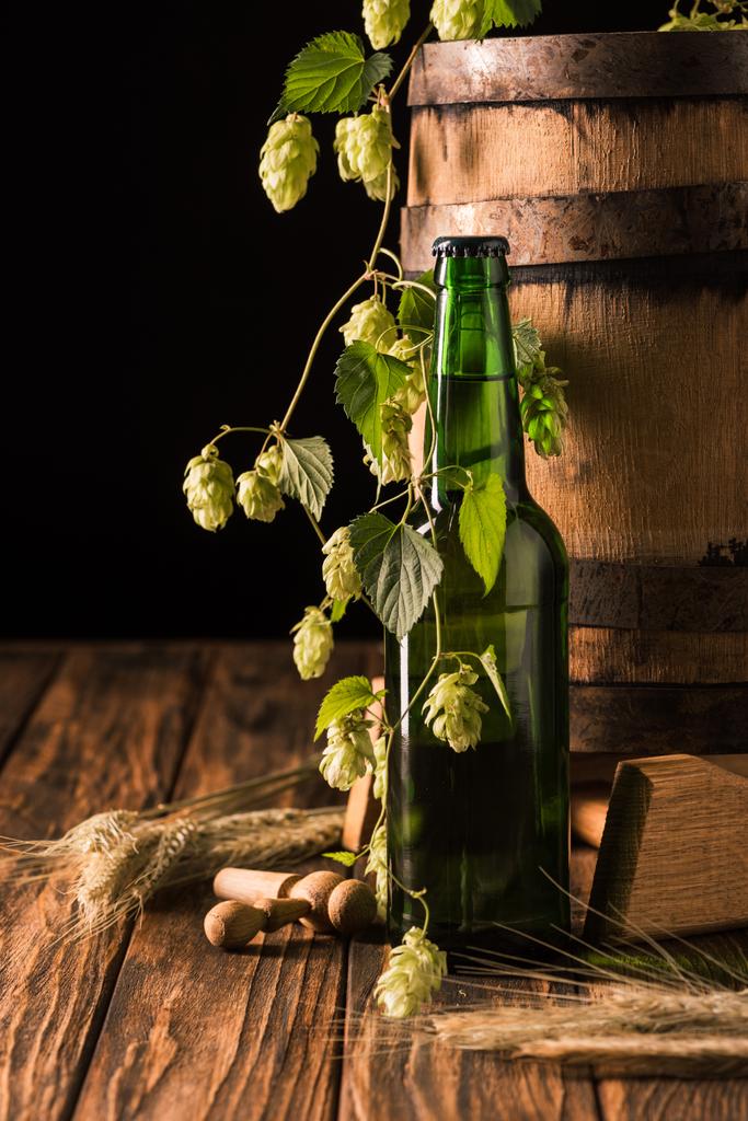 beer bottle, wheat, hop and wooden barrel at table on black background - Photo, Image