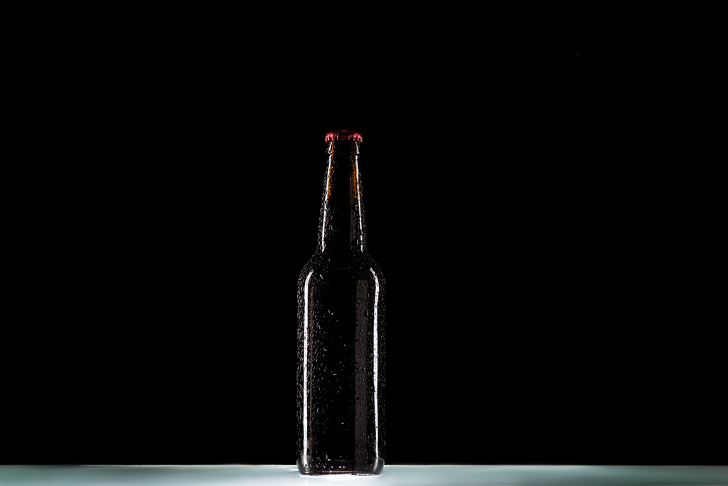 Close-up van bierfles op tafelblad op zwarte achtergrond, minimalistische concept - Foto, afbeelding