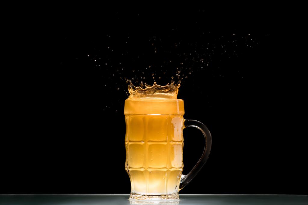 glas light bier met spatten aan tafel op zwarte achtergrond, minimalistische concept - Foto, afbeelding
