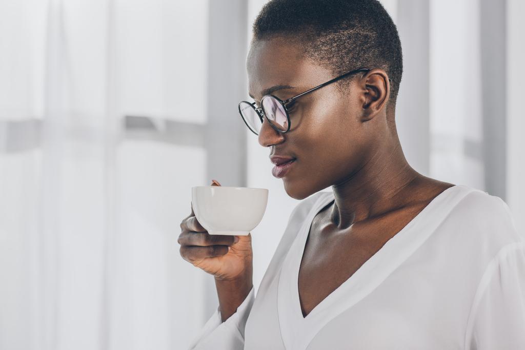 vista laterale di elegante attraente donna d'affari africana americana che beve caffè in ufficio
 - Foto, immagini