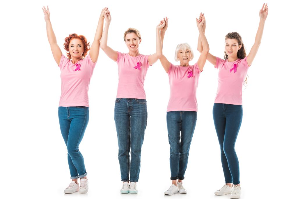 women with breast cancer awareness ribbons holding hands and smiling at camera isolated on white  - Photo, Image