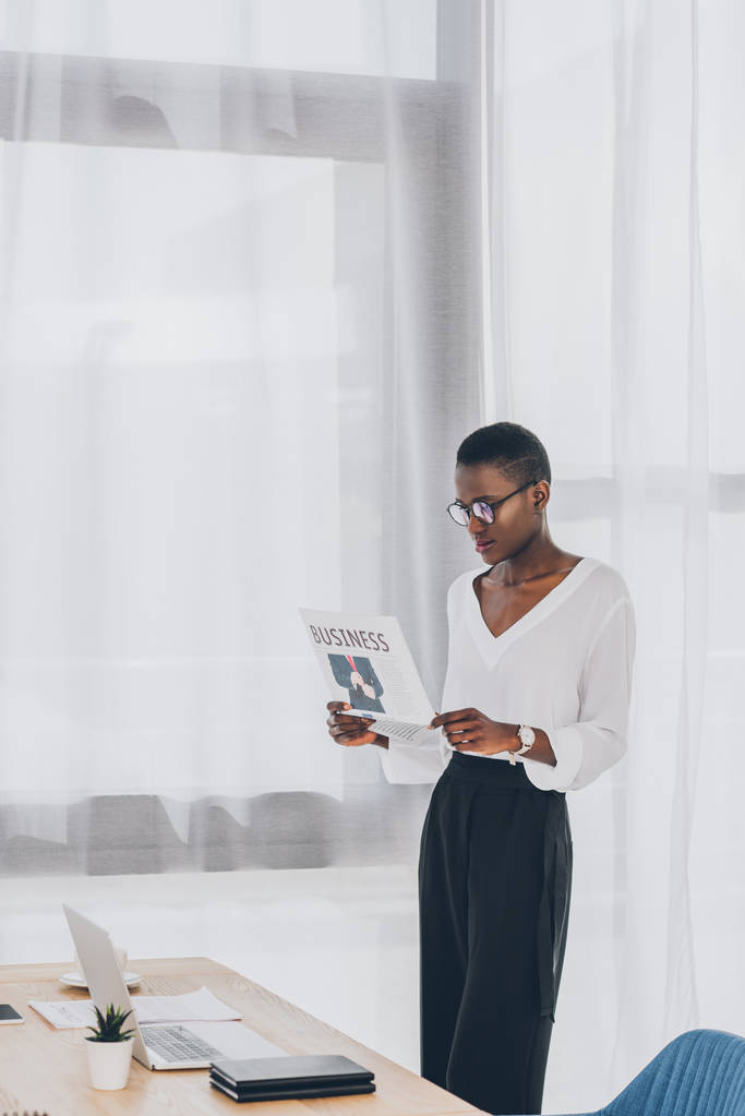 stylische attraktive afrikanisch-amerikanische Geschäftsfrau mit kurzen Haaren liest Zeitung im Büro - Foto, Bild