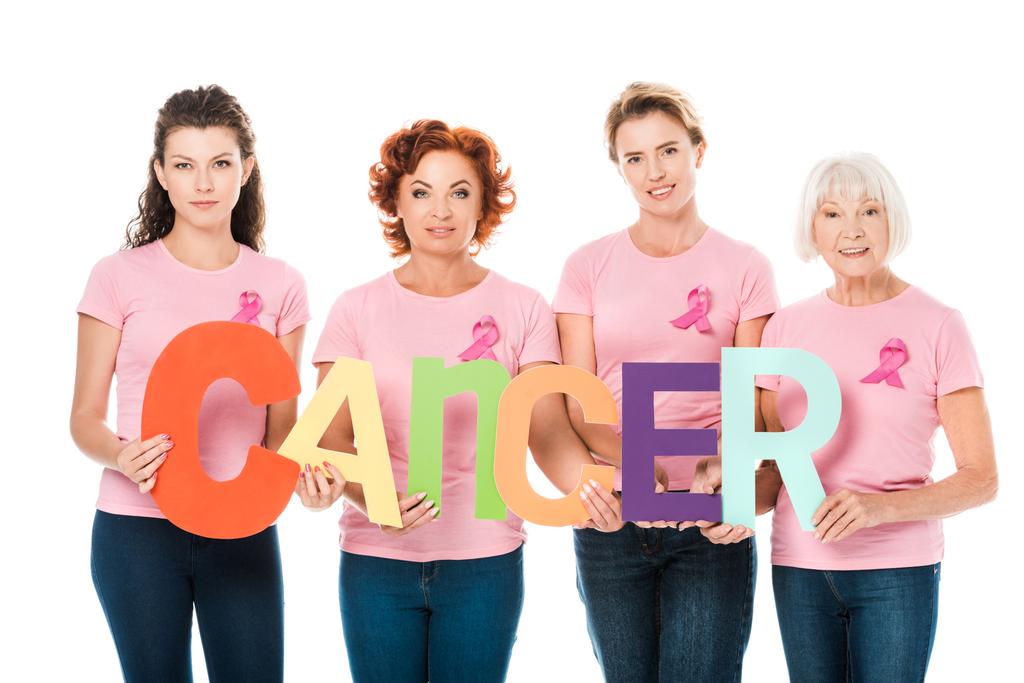 mujeres en camisetas de color rosa con cintas de conciencia de cáncer de mama con letras de colores con cáncer de palabra y sonriendo a la cámara aislada en blanco
  - Foto, Imagen