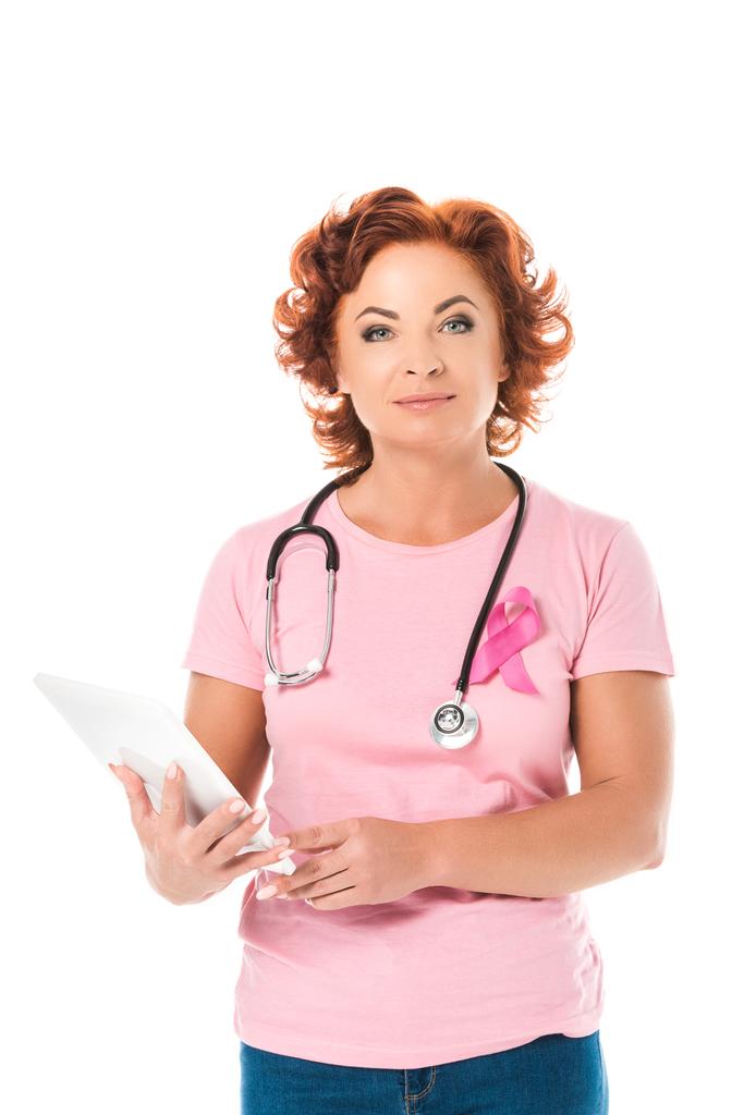 rijpe vrouw met stethoscoop digitale tablet houden en kijken naar camera geïsoleerd op wit, borst kanker bewustzijn concept - Foto, afbeelding