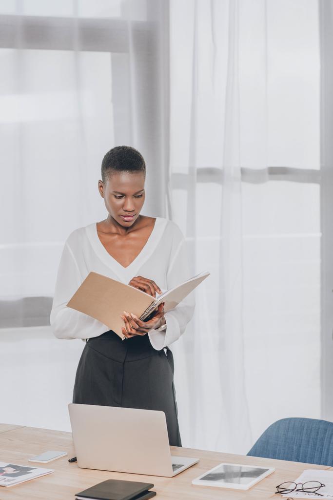 stylish attractive african american businesswoman looking in folder in office - Photo, Image