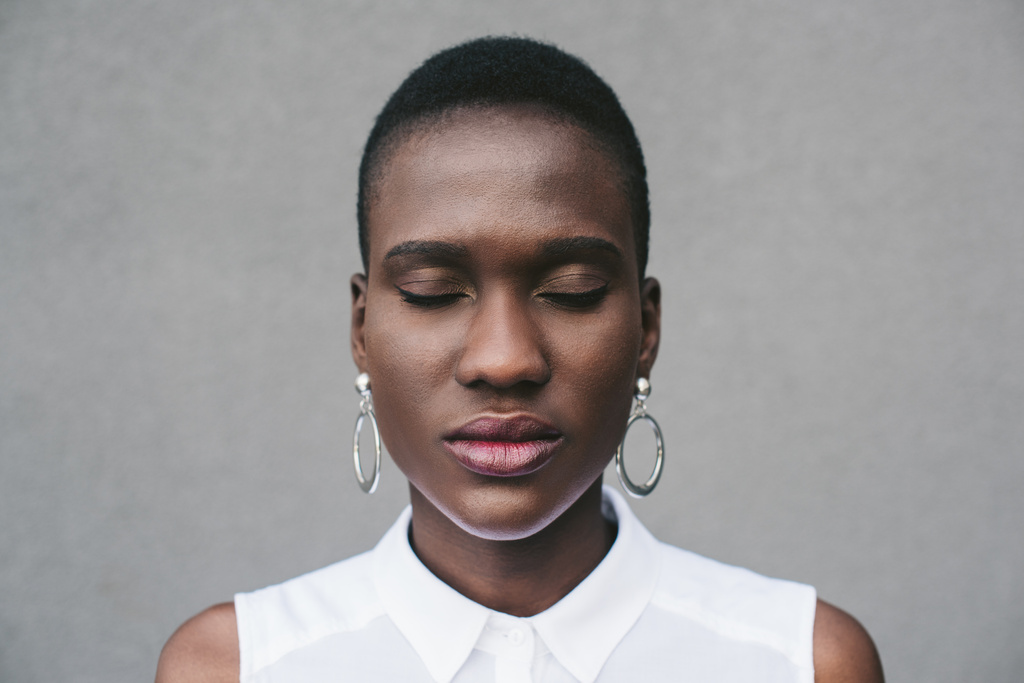 ritratto di elegante donna afro-americana attraente in piedi con gli occhi chiusi vicino al muro grigio
 - Foto, immagini