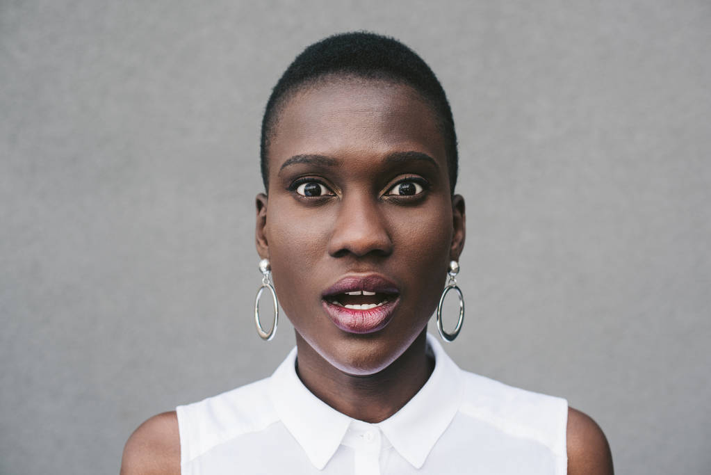 portrét překvapen stylové atraktivní afroamerické ženy při pohledu na fotoaparát šedé zdi - Fotografie, Obrázek