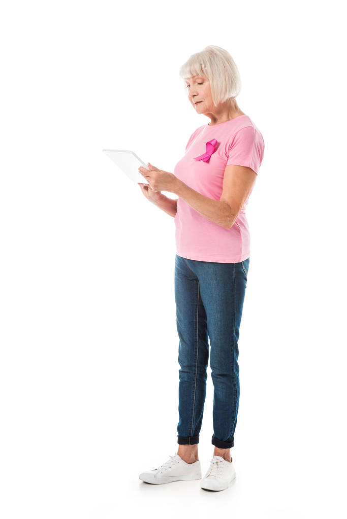 femme âgée en t-shirt rose avec ruban de sensibilisation au cancer du sein en utilisant une tablette numérique isolée sur blanc
  - Photo, image