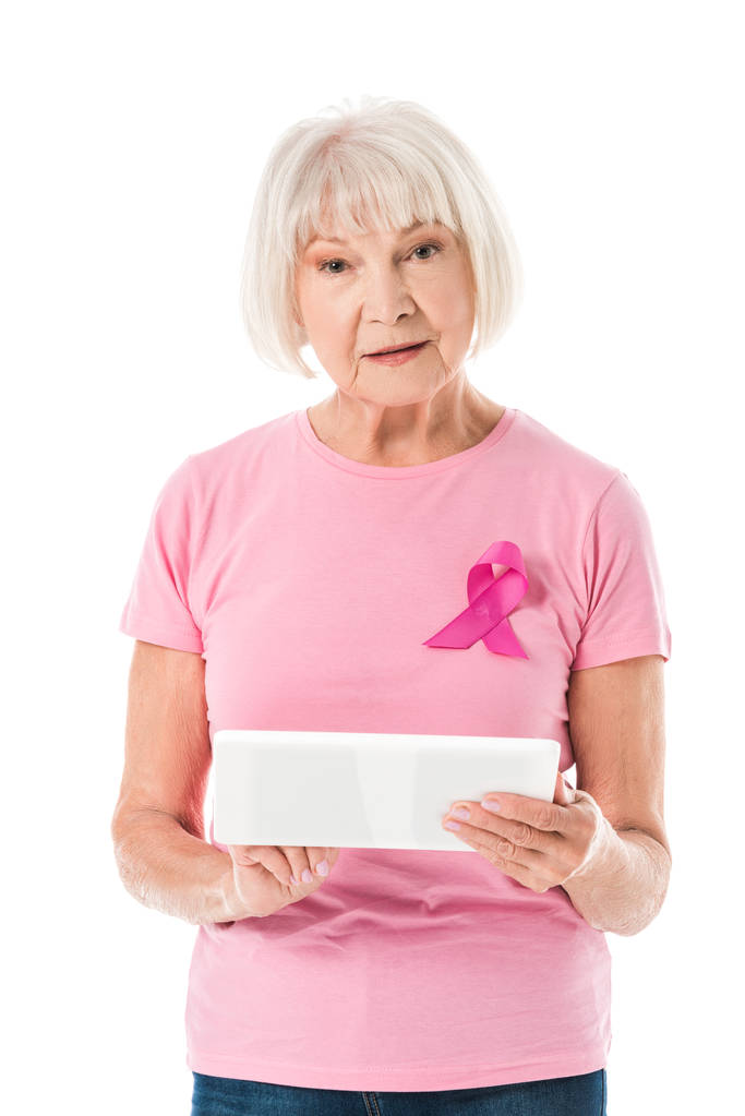 mujer mayor en camiseta rosa con cinta de conciencia de cáncer de mama que sostiene la tableta digital y mirando a la cámara aislada en blanco
  - Foto, imagen