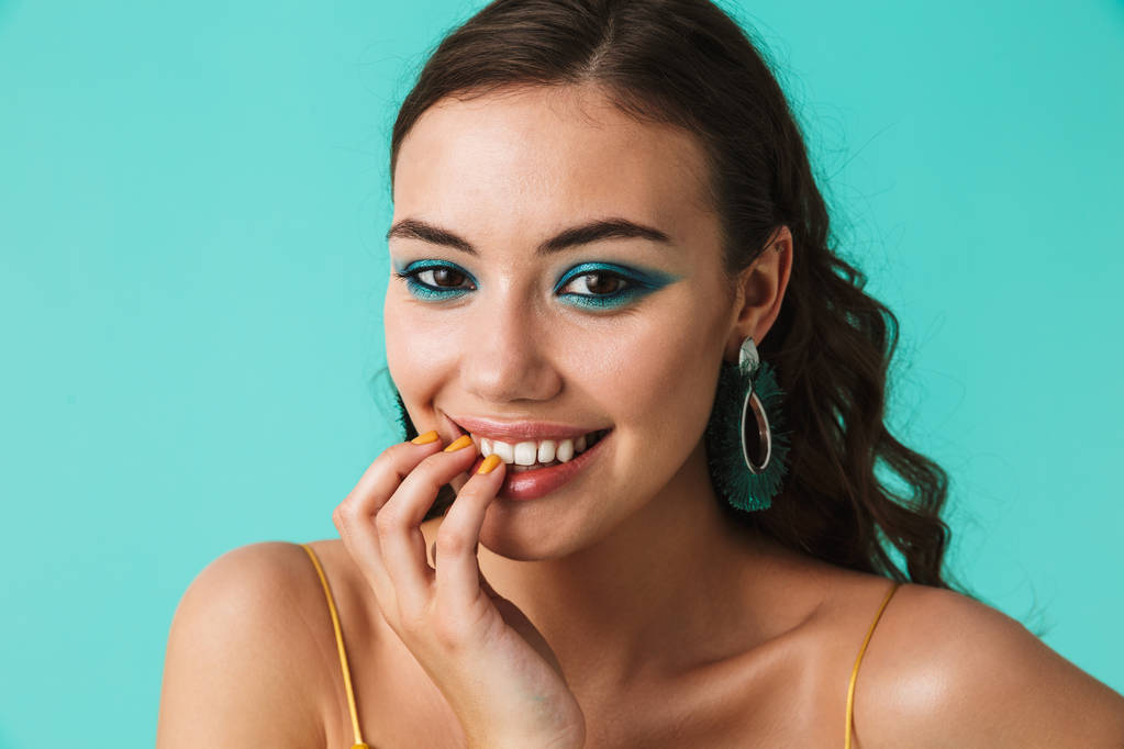 Vértes fotó imádnivaló lány 20s visel elegáns smink és fülbevaló mosolyogva kamera, elszigetelt, felett kék háttér - Fotó, kép