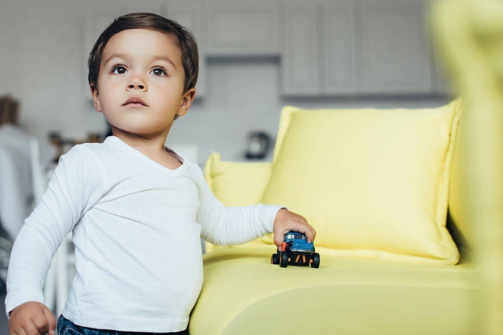 niño jugando con el coche azul del juguete en sofá
 - Foto, Imagen