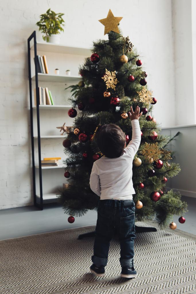 vista trasera del niño saludando al árbol de Navidad en casa
  - Foto, imagen
