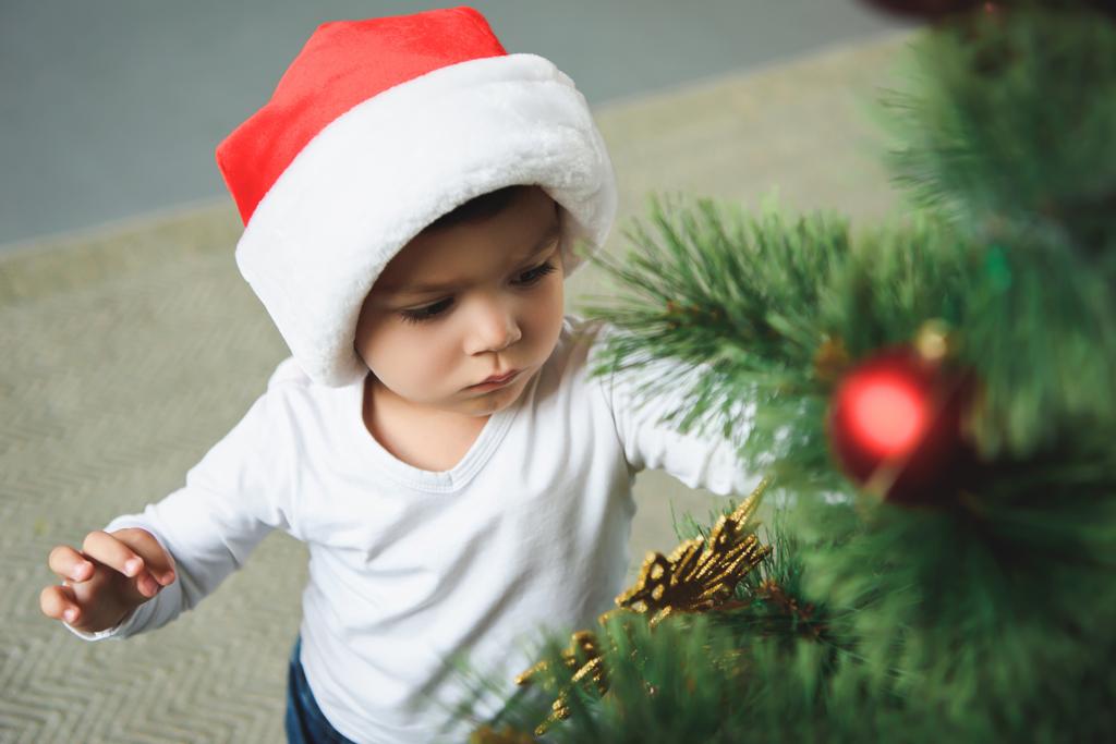 cute boy in red santa hat decorating christmas tree - Photo, Image