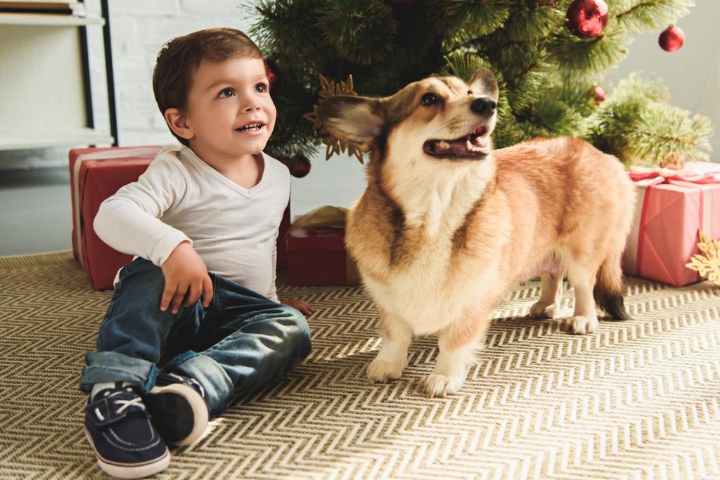 entzückender Junge und Hund sitzen unter Weihnachtsbaum mit Geschenken - Foto, Bild