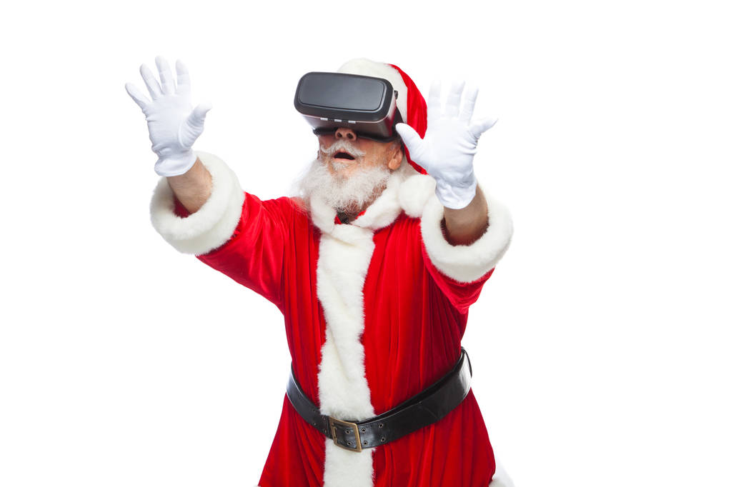 Рождество. Санта Клаус в черных очках виртуальной реальности делает жесты руками. Сюрприз, эмоции. Новые технологии. Изолированный на белом фоне
. - Фото, изображение