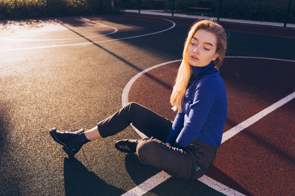 fiducioso modello ragazza bionda in un maglione blu in posa su un campo sportivo ai raggi del sole del mattino
 - Foto, immagini